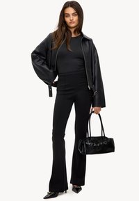 Chaqueta de cuero negra, top negro ajustado, pantalones negros acampanados, tacones negros de punta y un pequeño bolso negro. Diseño minimalista con texturas elegantes.