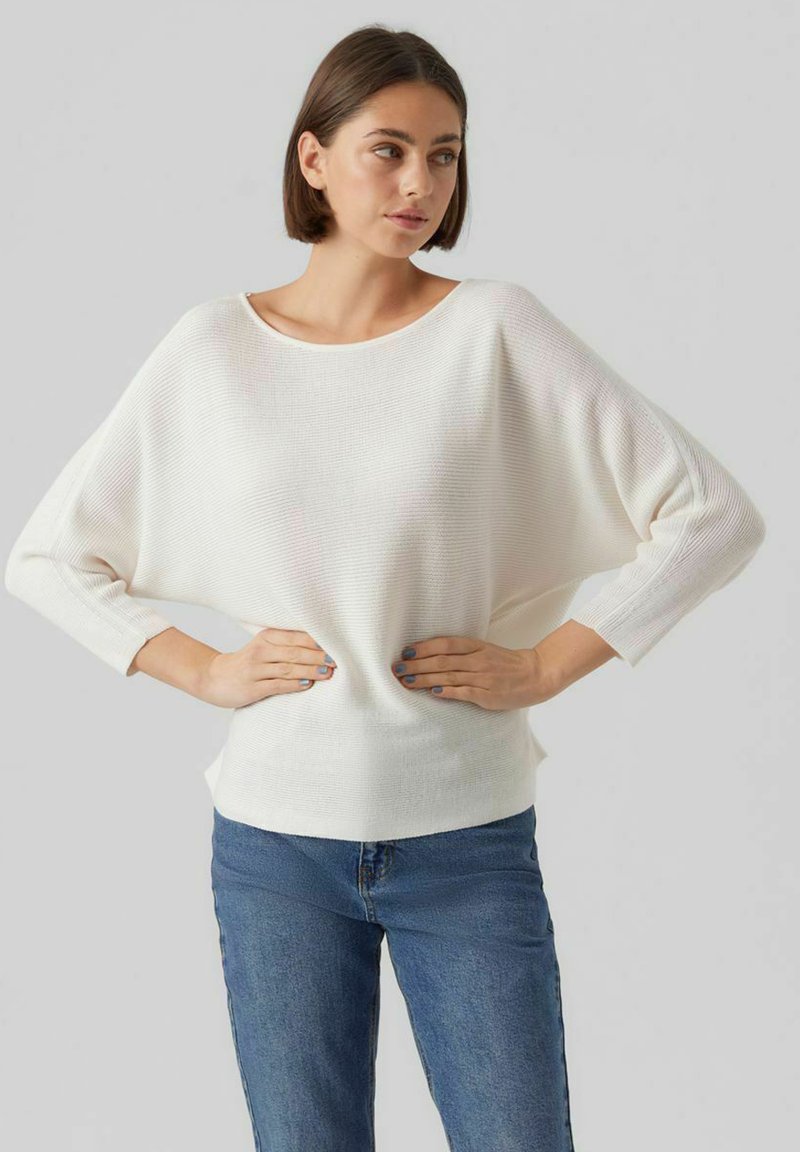 Weißer übergroßer Pullover mit geripptem Textil und weitem Boot-Ausschnitt. Mit Dreiviertelärmeln und lockerer Passform. Kombiniert mit Jeans.