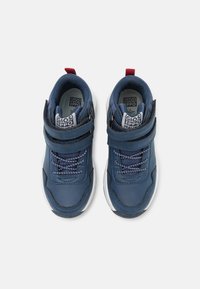 Zapatillas azul marino con parte superior de cuero suave, cuello acolchado, suela de goma blanca y correa ajustable sobre los cordones para un ajuste seguro.