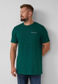 Groene T-shirt met ronde hals en korte mouwen, voorzien van een kleine witte opdruk "Abonneer je op de Natuur" op de borst en een losse pasvorm.