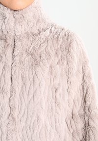 Ljusrosa fuskpälsjacka med hög krage, med ett strukturerat, vadderat mönster och mjuk, fluffig yta.