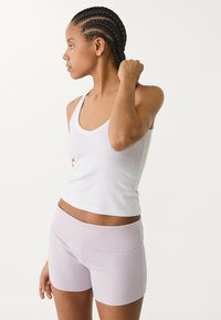 Weißes, figurbetontes Tanktop mit Rundhalsausschnitt, kombiniert mit helllila, hochtaillierten Shorts. Glatter, dehnbarer Stoff ohne sichtbare Muster.