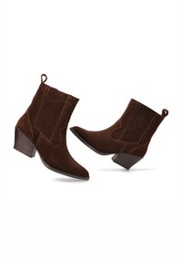 Botas de tobillo de ante marrón con punta afilada, paneles laterales elásticos y un tacón de 5 cm. Cuenta con un lazo para ponerlas y quitarlas fácilmente.