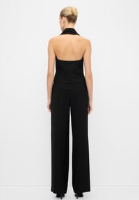 Schwarzes Halftertop mit weißen Punkten, kombiniert mit hoch taillierten schwarzen Hosen mit seitlichen Verzierungen, von hinten gezeigt.
