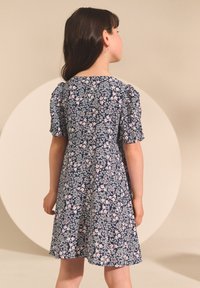 Abito blu navy a fiori con maniche corte a sbuffo, motivo floreale rosa e bianco, gonna svasata e scollatura rotonda, visto da dietro.