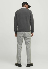 Grau gestrickter Pullover mit gerippten Bündchen und Saum, kombiniert mit hellgrauen Hosen und schwarzen Schuhen. Die Rückansicht zeigt die gesamte Passform.