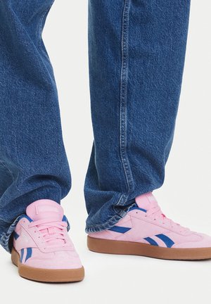 Różowe zamszowe trampki z niebieskimi paskami, gumowymi podeszwami i miękką fakturą. W zestawie z luźnymi, niebieskimi spodniami dżinsowymi.