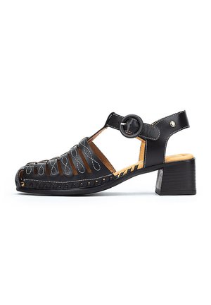 Sandalia de cuero negro con diseño perforado, tira para el tobillo con hebilla circular y tacón bajo. Plantilla de color marrón claro con detalles de costura.