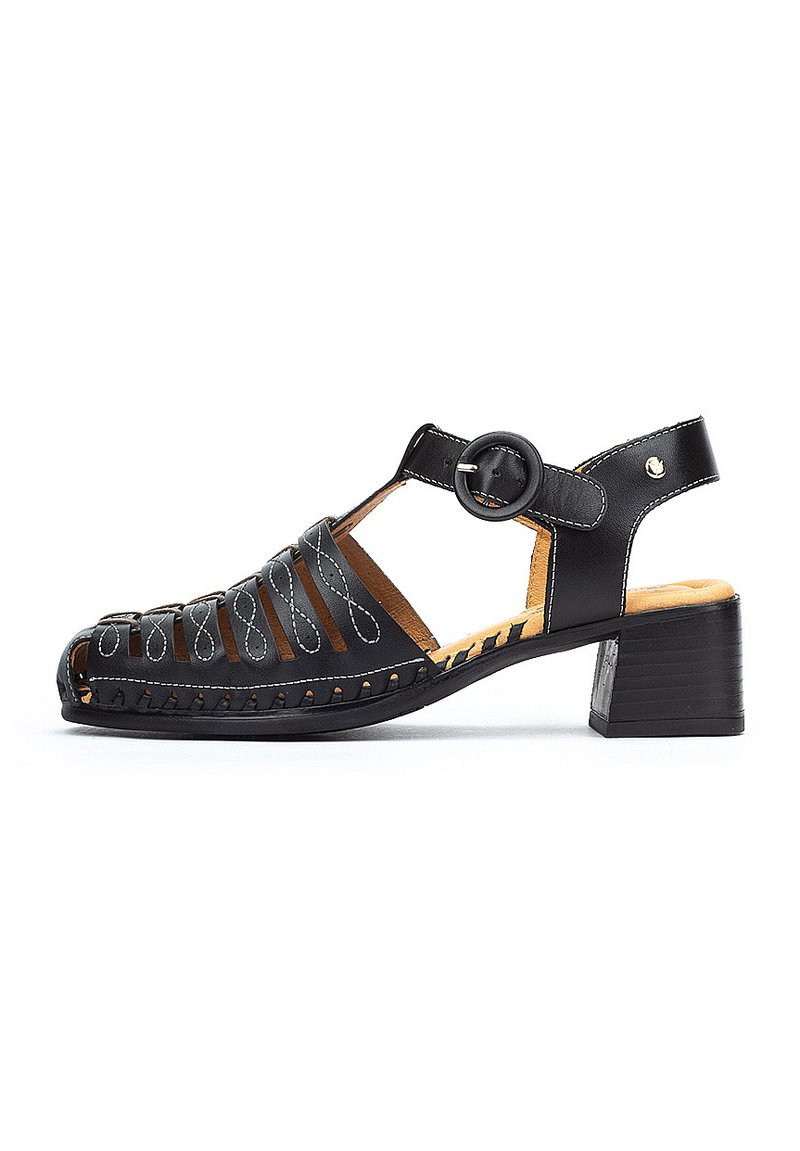 Sandalia de cuero negro con diseño perforado, tira para el tobillo con hebilla circular y tacón bajo. Plantilla de color marrón claro con detalles de costura.