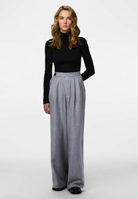 Czarny prążkowany top z golfem w połączeniu z jasnoszarymi spodniami o wysokim stanie i plisami, zdobionymi guzikiem, o luźnym, szerokim kroju.