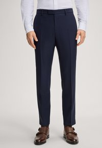 Pantaloni sartoriali blu navy con pieghe, realizzati in tessuto liscio. Presentano una parte anteriore piatta, passanti per cintura e una vestibilità slim sotto una camicia leggera a motivo.