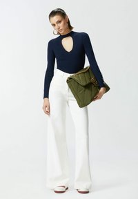 Body in tessuto a coste blu navy con scollatura a chiave, abbinato a pantaloni bianchi a vita alta e gamba larga e a una borsa trapuntata verde con hardware dorato.