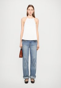 Weißes ärmelloses Halfter-Top, hellblaue verwaschene Jeans mit Stickerei, schwarze Ballerinas und eine kleine braune Handtasche.