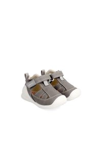 Scarpe in tessuto grigio con suole in gomma bianche, dotate di una tracolla in Velcro e design forato per la ventilazione. Punta arrotondata e costruzione leggera.