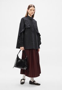 Črna srajca z nabranimi rokavi in detajlom kravate; bordo plise krilo; črna usnjena torbica; črni balerini z belimi nogavicami; minimalističen slog.