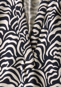 Et tæt billede af stof, der har et mønster af sorte og cremefarvede zebra-striber, med en V-halsudskæring og synlige syninger.