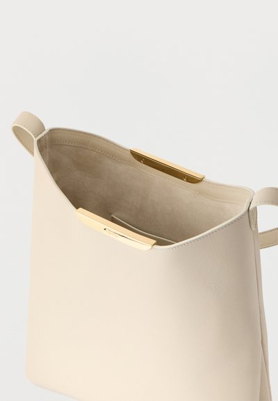 Τσάντα χειρός από δέρμα κρεμ με χρυσά κούμπωμα, ανοιχτό πάνω μέρος που αποκαλύπτει το εσωτερικό από σουέτ μπεζ και μικρή εσωτερική τσέπη.