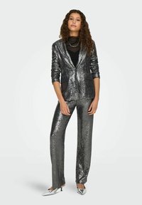 Conjunto de blazer y pantalón de lentejuelas en negro y plata brillante. El blazer tiene solapas en pico y dos bolsillos delanteros. Pantalones ajustados con un ligero acampanado.