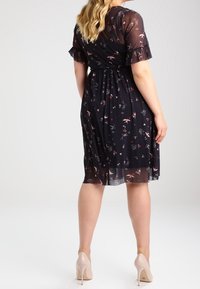 Svart blommig klänning med korta, fransiga ärmar, åtsittande midja och genomskinlig överdel. Har ett mönster av små blommor i rosa och vitt.