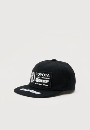 Черна шапка с плоска козирка и кръпка с логото на Toyota Land Cruiser и HUF, показана на изчистен светъл фон.