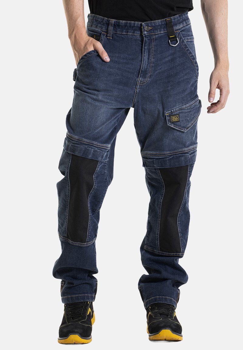 Pantalons cargo en denim avec des panneaux de tissu foncé, plusieurs poches et une coupe décontractée. La taille comprend une boucle et des accents de passant de ceinture.