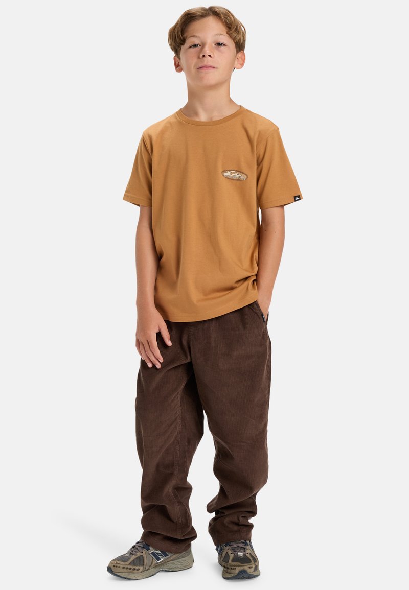 Camiseta de algodón marrón con mangas cortas y parche de logo, combinada con pantalones de pana marrón oscuro. Corte casual, estilo relajado y tejido texturizado.
