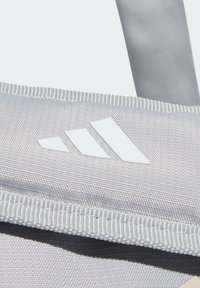 Harmaa kangaskassi, jossa valkoinen Adidas-logo, näkyvillä tikkaus ja sileä pinta. Mallissa on vetoketju ja tasaiset hihnat.