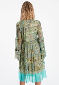 Langärmliges, grün gemustertes Kleid mit gestuften Design, durchsichtigem Stoff und türkisfarbener Säume. Mit floralen und Paisleymotiven.