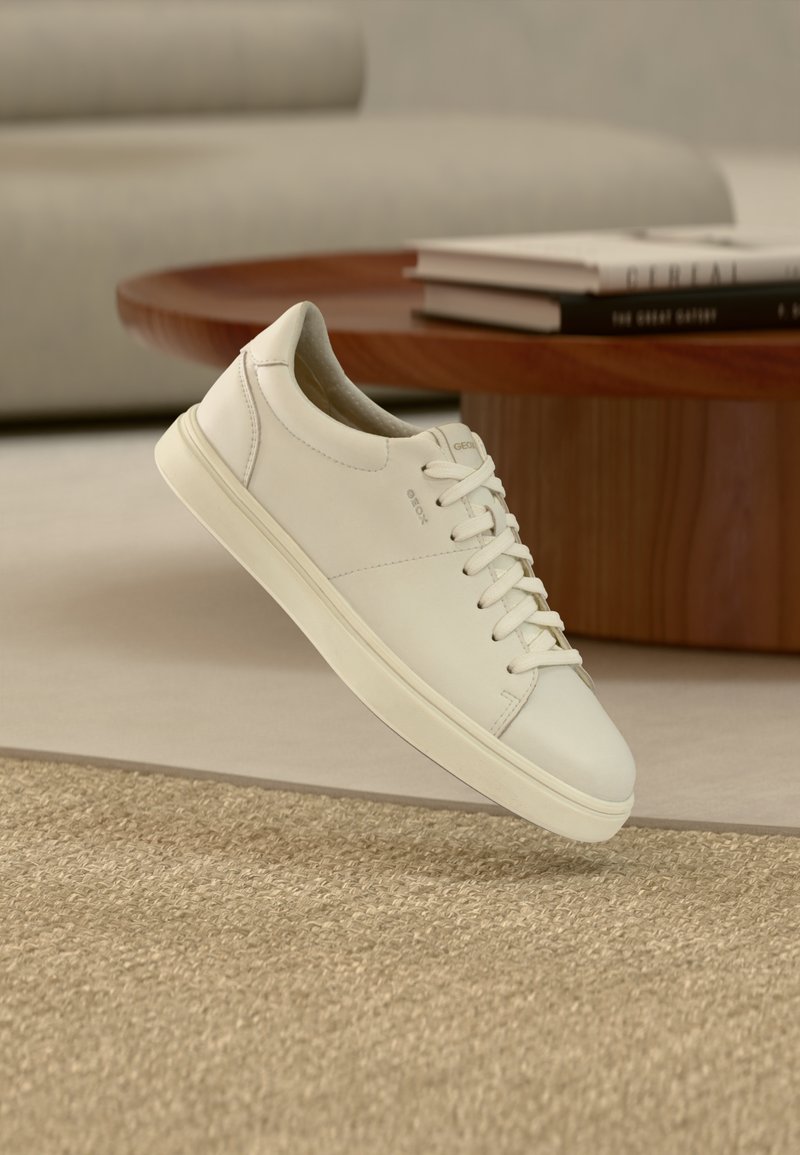 Λευκό δερμάτινο αθλητικό παπούτσι με λεία υφή, στρογγυλή μύτη και επίπεδα κορδόνια. Διαθέτει διακριτικό λογότυπο και ελαφριά σόλα.