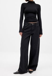 Črne široke jeans hlače z teksturiranim vzorcem majhnih pikic, ki vsebujejo klasičen pet-pocket dizajn in zatič za zapiranje v pasu.