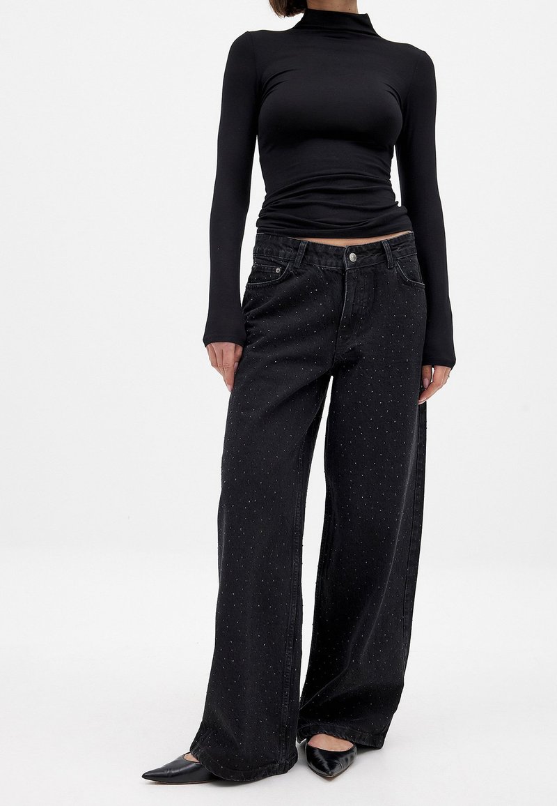 Črne široke jeans hlače z teksturiranim vzorcem majhnih pikic, ki vsebujejo klasičen pet-pocket dizajn in zatič za zapiranje v pasu.