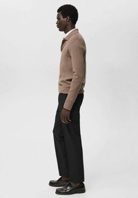 Suéter polo de punto marrón, pantalones negros y mocasines negros. Textura suave, diseño ajustado y cuello con botones.