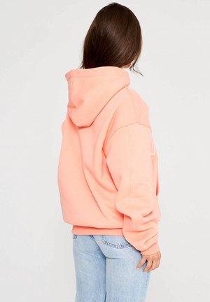 Sudadera con capucha rosa de corte relajado, con puños y dobladillo de canalé, hecha de material de algodón suave. Llevada con jeans de color azul claro.