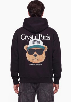 Person wearing a black hoodie with a bear graphic wearing sunglasses and a cap, text reads Crystal Paris and Summer 2026 on the back.