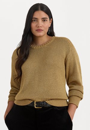 Stickad tröja i dämpad guldnyans med ribbad halsringning och muddar. Parerad med ett svart vävt bälte med ett guldspänne, burren över svarta byxor.