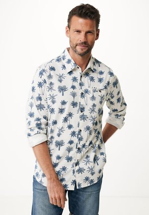 Camisa de manga corta y con botones de tejido ligero, con un fondo blanco y patrones de palmeras en azul oscuro. Cuello clásico y mangas enrolladas.