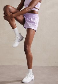 Pantalones cortos deportivos de color púrpura claro con cintura elástica, combinados con calcetines blancos y zapatos blancos Nike, que muestran un diseño elegante y una textura suave.