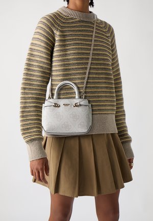 Osoba ubrana w beżowy sweter w paski i brązową plisowaną spódnicę, niosąca małą białą torebkę designerską na łańcuszku noszoną przez ramię.