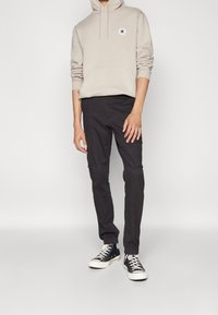 Beige huvtröja med framficka och logotyp, kombinerad med svarta cargobyxor med sidofickor och svarta höga sneakers.