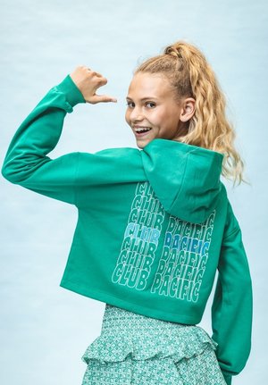 Groene cropped hoodie met een grote grafische tekstontwerp in blauw en wit, gecombineerd met een gestreepte rok met ruches.