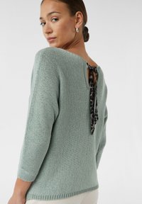 Mintgrüner Strickpullover mit drei Viertelärmeln, ausgestattet mit einem Leopardenmuster-Knoten am Rücken und gerippten Bündchen sowie Saum.