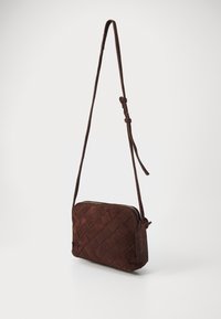 Brun ruskinds crossbody taske med vævet tekstur, slank design og lynlås-lukning. Har en justerbar rem og afrundede kanter.