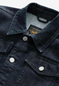 Dark denim jacket featuring a pointed collar, silver buttons, two chest pockets, and a textured finish on the fabric.