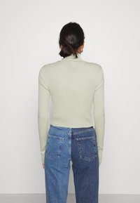 Ribbad, ljusgrön polotröja med långa ärmar, kombinerad med högmidjade, tvåtonade blå denimjeans. Slät textur och figursydd design.