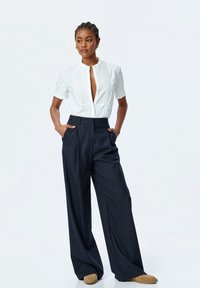 Witte blouse met korte mouwen, een kraag en knoopsluiting, gecombineerd met marineblauwe brede gestreepte broek en lichtbruine instappers.
