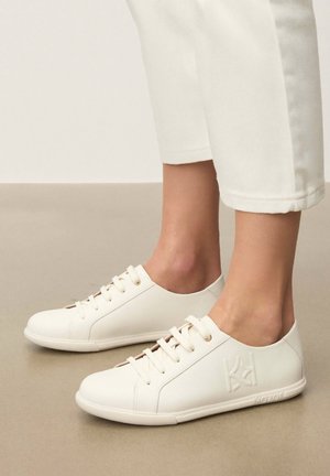 Valged nahast vabaajajalatsid ümarate varvastega, kuue aasaauguga ja kõrgenenud brändinguga küljel. Sile tekstuur peene õmbluse detailiga.