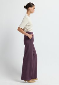 Haut en crème avec des manches courtes et un col en perles ; pantalon large texturé violet avec poches ; des talons beiges complètent le look.