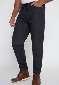 Pantaloni jogger neri con elastico in vita e cordino, dotati di tasche laterali e polsini affusolati, abbinati a stivali marroni con lacci.