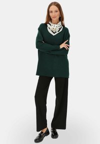 Ciemnozielony, oversize'owy sweter o prążkowanej fakturze, zestawiony z szerokimi czarnymi spodniami. Uzupełniony białą chustą w kropki i błyszczącymi czarnymi butami.