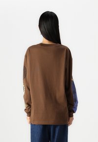 Ruskea pitkähihainen t-paita, jossa on rento malli. Ominaisuuksiin kuuluu pyöreä kaula-aukko ja kuvitettu koriste hihansuissa; pehmeää puuvillamateriaalia.